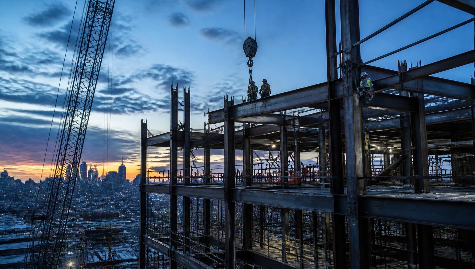 Structural steel high-rise frame with ironworkers against a dusk skyline